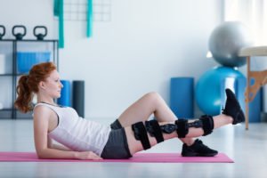 Sportswoman on mat doing exercises with broken leg during rehabilitation