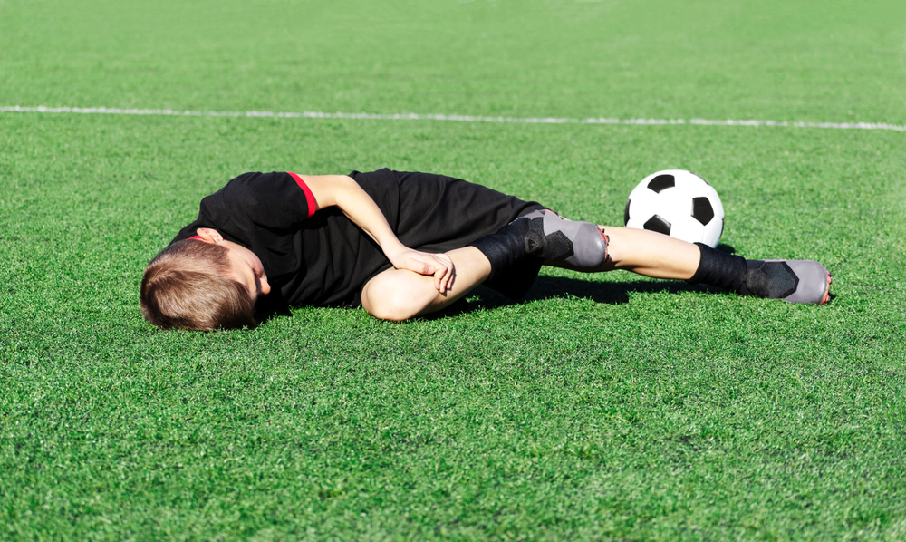Choroba Osgood-Schlattera - Młody chłopiec leżący na boisku, trzymający się za kolano - brandvital.eu